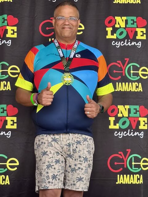 Anthony Brown with his finisher's medal in front of a Cycle Jamaica backdrop